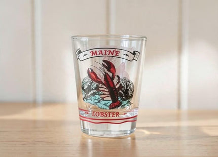 Maine Shot Glass - Lobster / Ocean — small empty souvenir shot glass in a cottage setting, Seasonal Maine logo