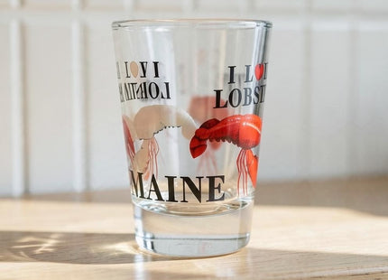 Maine Shot Glass - I love Lobster — small empty souvenir shot glass in a cottage setting, Seasonal Maine logo