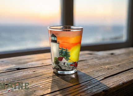 Maine Shot Glass - Lighthouse — small empty souvenir shot glass in a cottage setting, Seasonal Maine logo