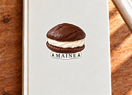 Maine Whoopie Pie Vinyl Sticker – 3 Inch shown on a notebook in a styled setting, with Seasonal Maine logo. Includes sticker only.