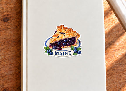Maine Blueberry Pie Vinyl Sticker – 3 Inch shown on a notebook in a styled setting, with Seasonal Maine logo. Includes sticker only.