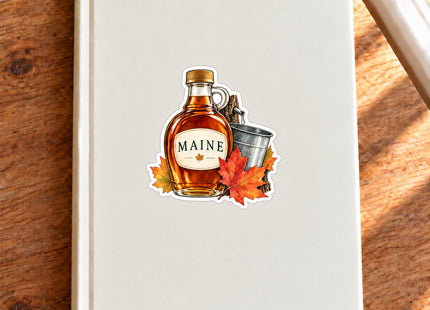 Maine Maple Syrup Vinyl Sticker – 3 Inch shown on a notebook in a styled setting, with Seasonal Maine logo. Includes sticker only.