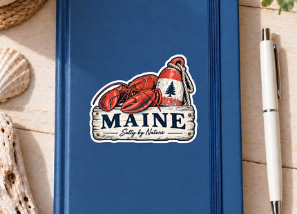 Maine Salty by Nature Lobster and Buoy Vinyl Sticker – 3 Inch shown on a notebook in a styled setting, with Seasonal Maine logo. Includes sticker only.