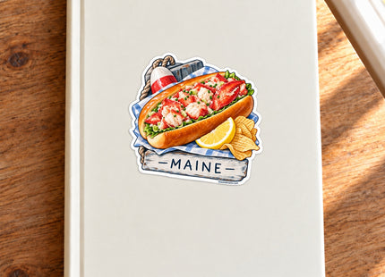 Maine Lobster Roll Vinyl Sticker – 3 Inch shown on a notebook in a styled setting, with Seasonal Maine logo. Includes sticker only.