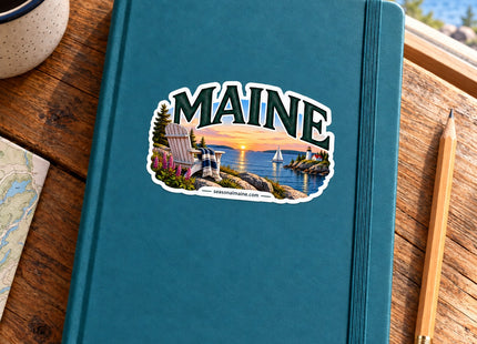 Maine Sunset Adirondack Chair Vinyl Sticker – 3 Inch shown on a notebook in a styled setting, with Seasonal Maine logo. Includes sticker only.
