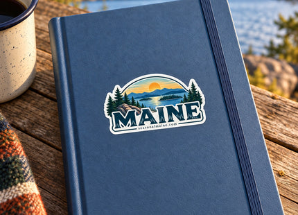 Maine Sunset Lake Landscape Vinyl Sticker – 3 Inch shown on a notebook in a styled setting, with Seasonal Maine logo. Includes sticker only.