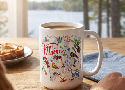 Maine State Collection ceramic mug with coffee on a wooden cottage table overlooking a lake; Seasonal Maine logo watermark