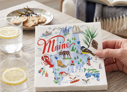Maine State Collection paper cocktail napkins beside sparkling water on a cottage table; Seasonal Maine logo watermark